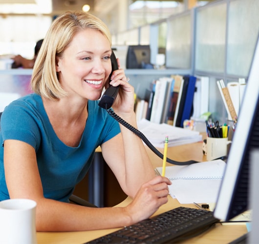 A blonde woman smiles while speaking on the phone.