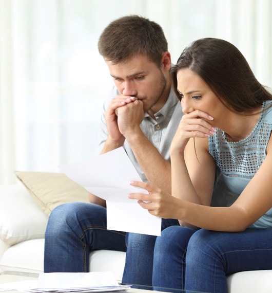 A couple sit on the couch, concerned over a document.