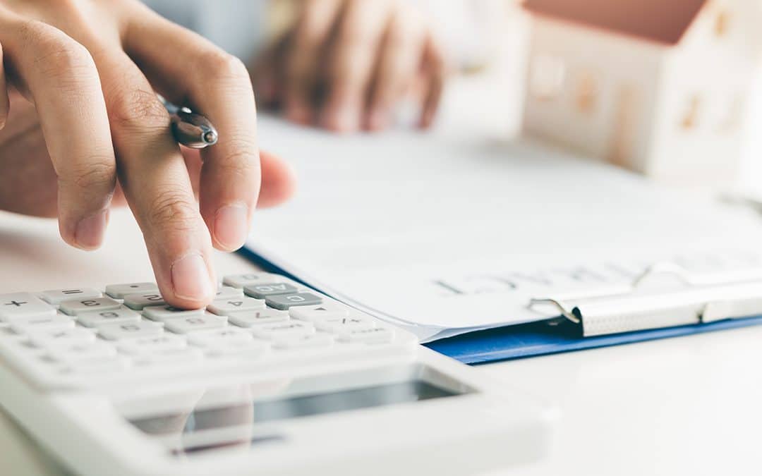 A hand holding a pen types on a calculator