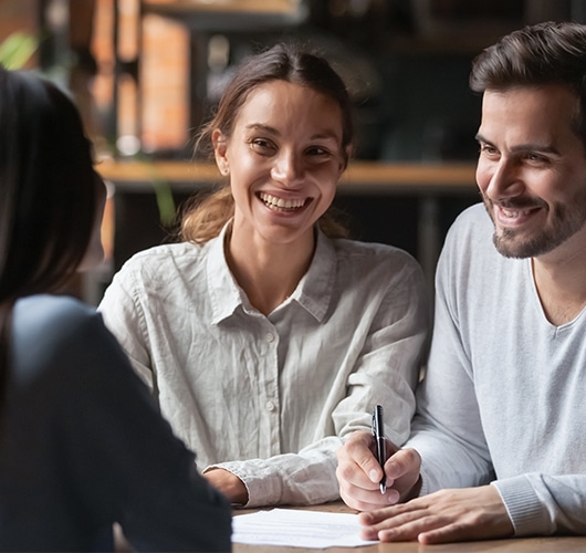 A smiling couple gets ready to sign a series of documents.